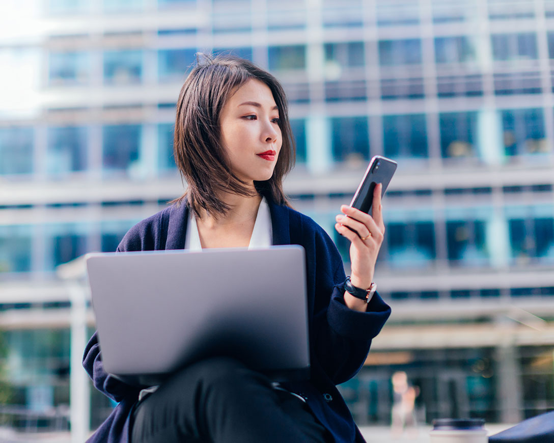 Ottimizzazione - Una donna d'affari che lavora su un laptop e uno smartphone all'aperto nel distretto finanziario