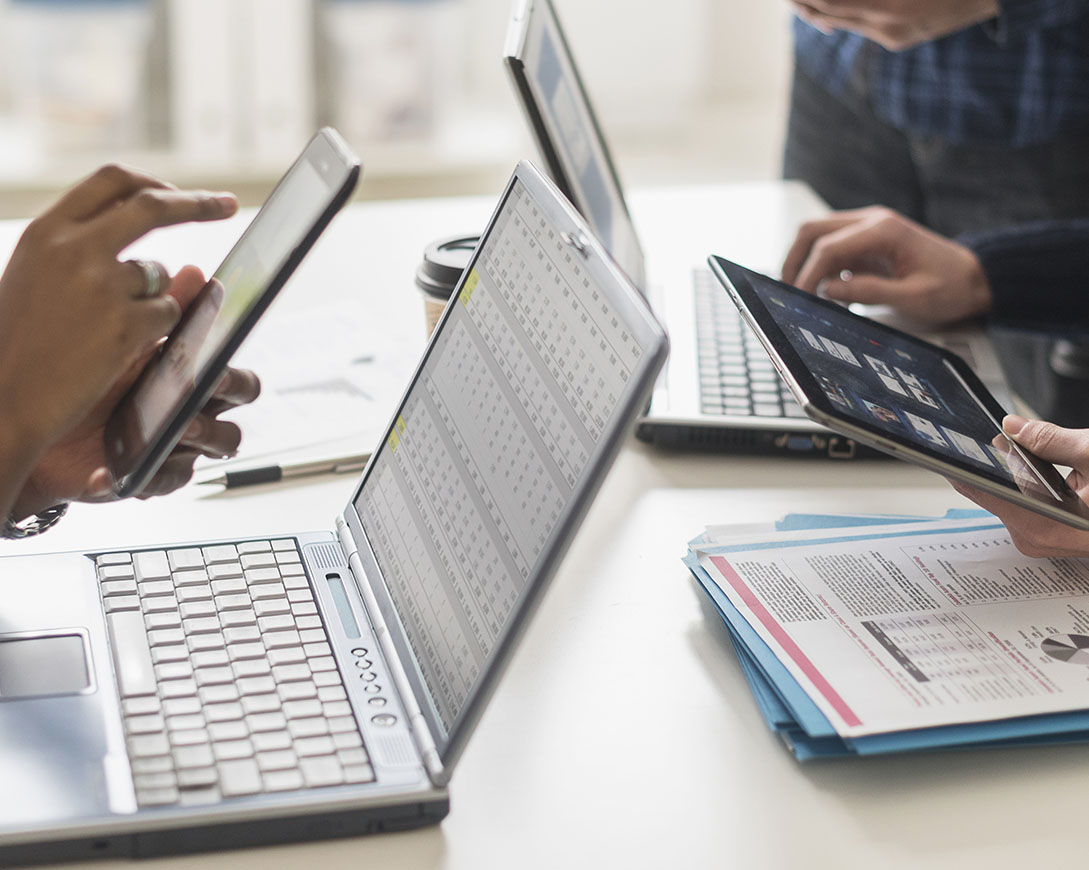 Ontap – Colleagues work at a table on a variety of devices: laptop, tablet, phone