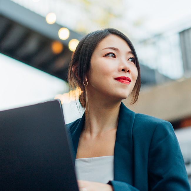 A woman working on a laptop outdoors in an urban setting glances to the side