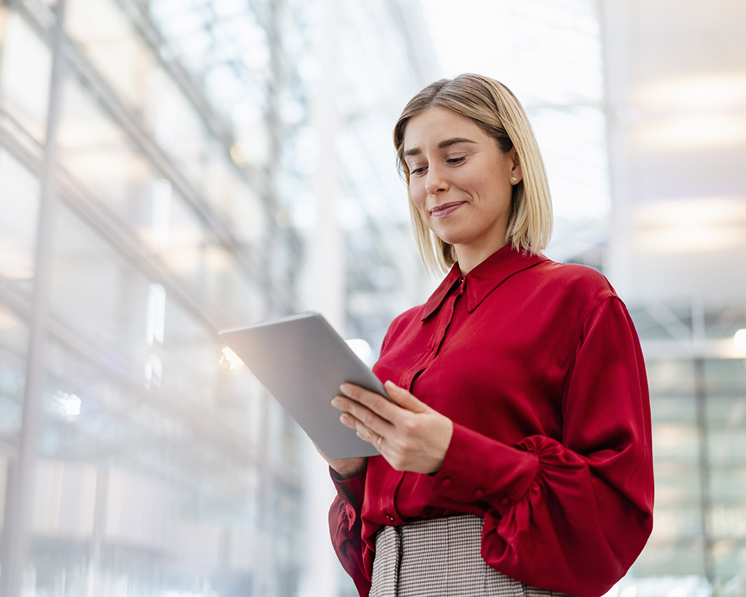 Integrated Solutions - A woman stands in a bright lobby, evaluating information on a laptop and happy about what she sees