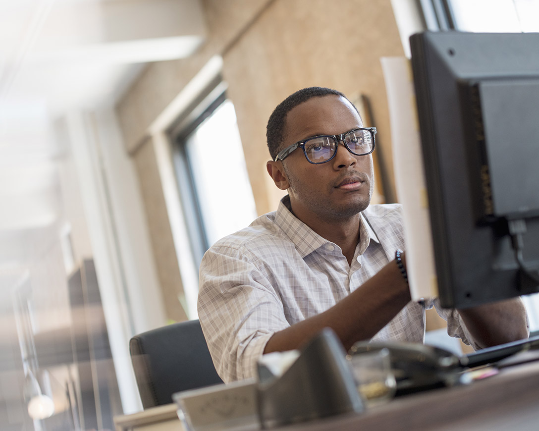 Performance - A man seated at a desk focuses on his monitor