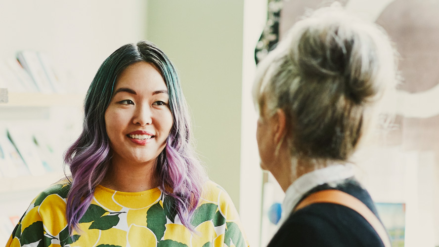 Due donne che conversano, una delle quali ha i capelli di un vivace colore viola.