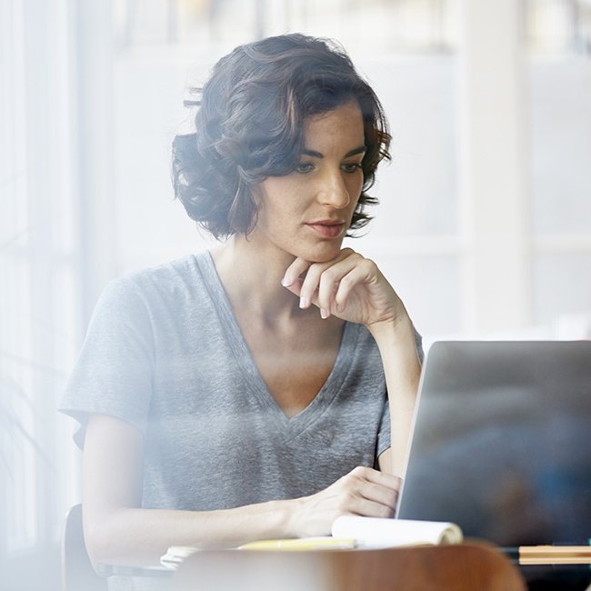 Una donna in un ambiente luminoso siede concentrata sul suo computer portatile