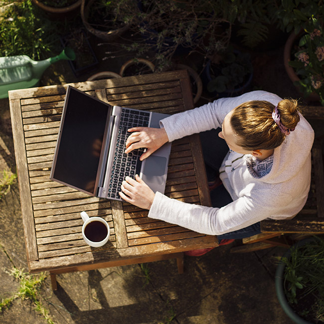 Frau, die an einem Laptop arbeitet und an einem kleinen Holztisch im Innenhof sitzt