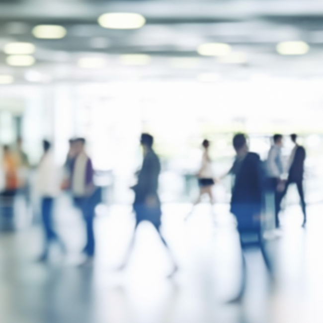 Viele unscharfe Menschen gehen durch eine helle Lobby in einem Bürogebäude, in dem ein geschäftiges Arbeitsumfeld herrscht