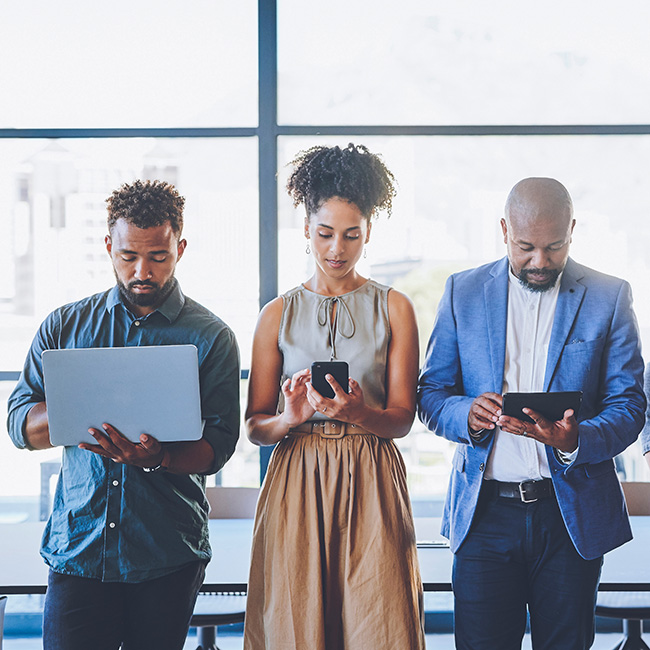 Tres personas trabajando codo con codo en distintos dispositivos