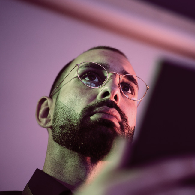 A man standing in a dimly lit room with a red light illuminating him from behind.