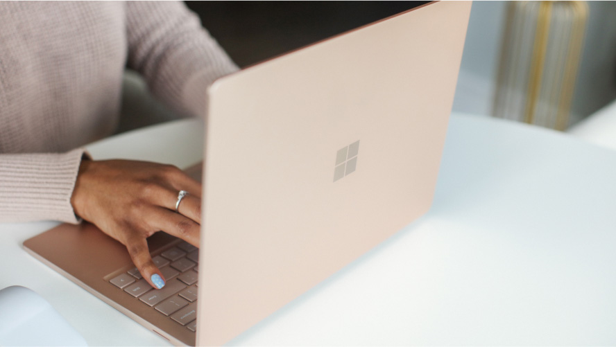 Mulher digitando no teclado de um laptop Microsoft Surface.