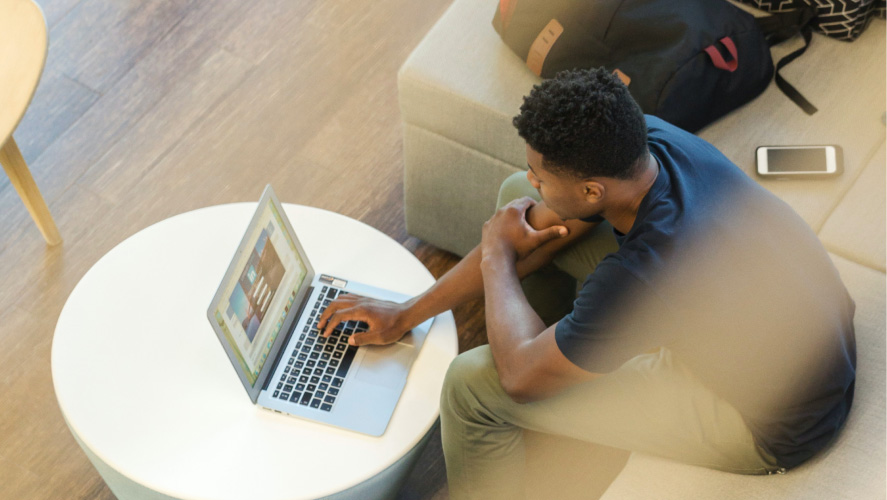 Um homem absorto no trabalho em um sofá, usando seu laptop para realizar tarefas de forma eficiente e confortável.