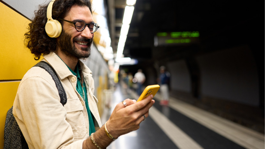 Un homme portant des écouteurs et tenant un téléphone jaune, absorbé par un contenu audio ou une communication.