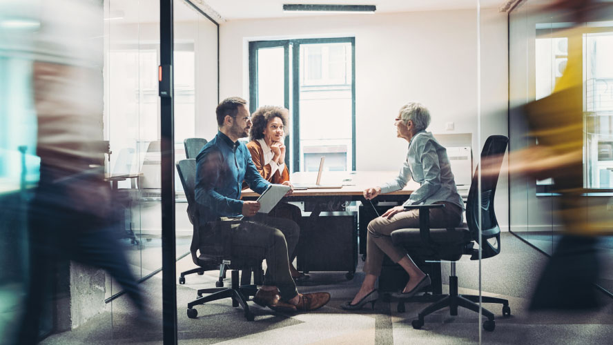 Reunião de negócios com três pessoas em uma mesa de conferência em um escritório.