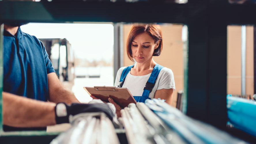 Woman in blue overalls holding clipboard next to man in blue shirt.