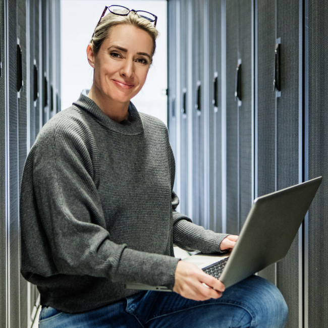 Mulher trabalhando em uma sala de servidores com um laptop.