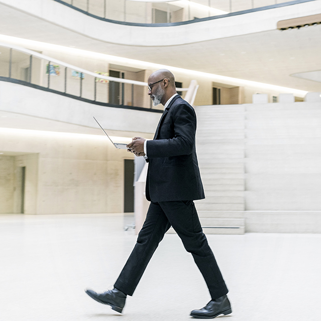 Businessman walking through a spacious foyer, looking at his laptop