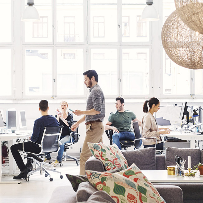 Three workers have a conversation while others focus on their tasks in an office environment