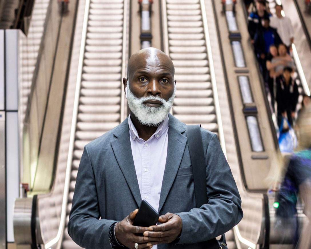 Homme à barbe grise debout devant un escalator.