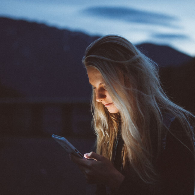 Una donna assorta nello schermo del suo telefono, affascinata dal suo bagliore, mentre l&#039;oscurità la circonda durante la notte.