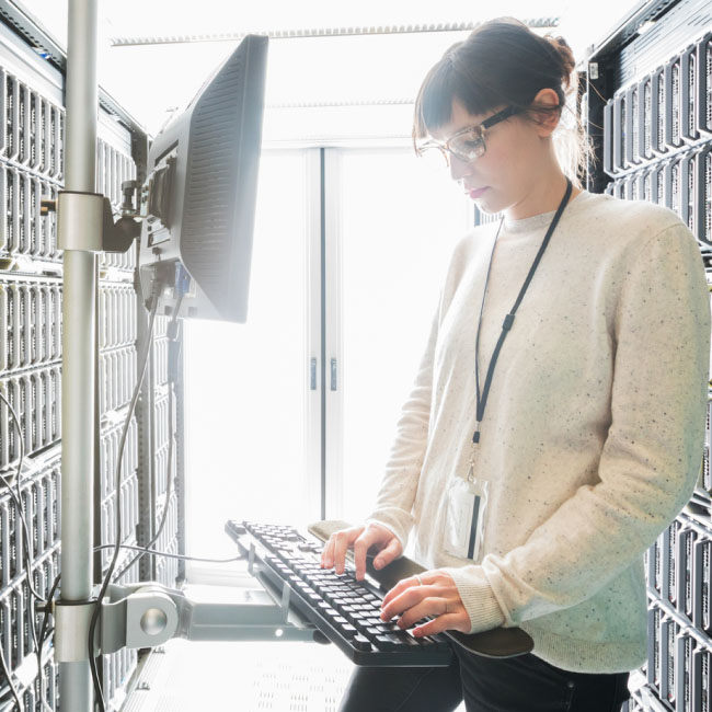 Female IT professional typing on keyboard in server room.