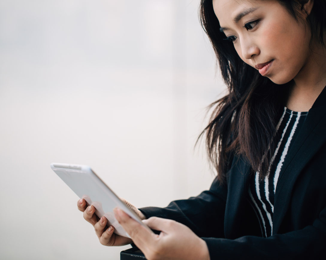 An Asian woman engrossed in work, utilizing a tablet computer in a professional office setting.