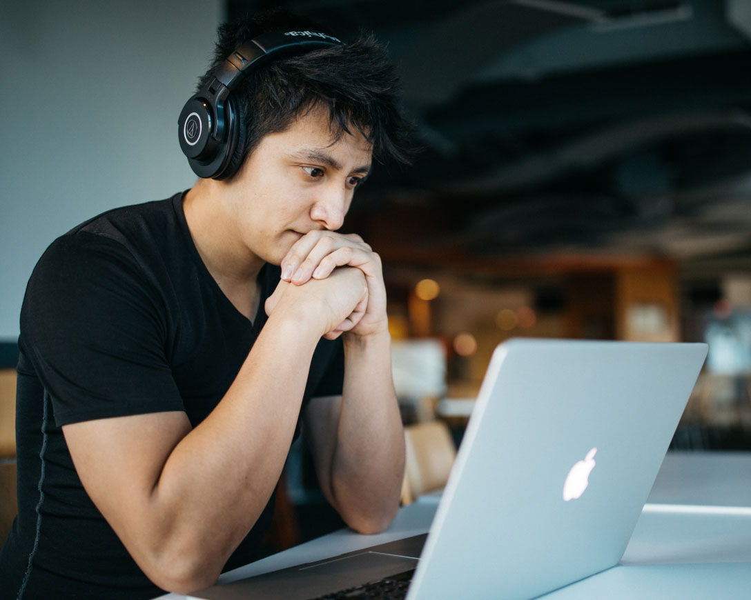 A man engrossed in work, wearing headphones, sits at a table with his laptop, focused and immersed in his tasks.