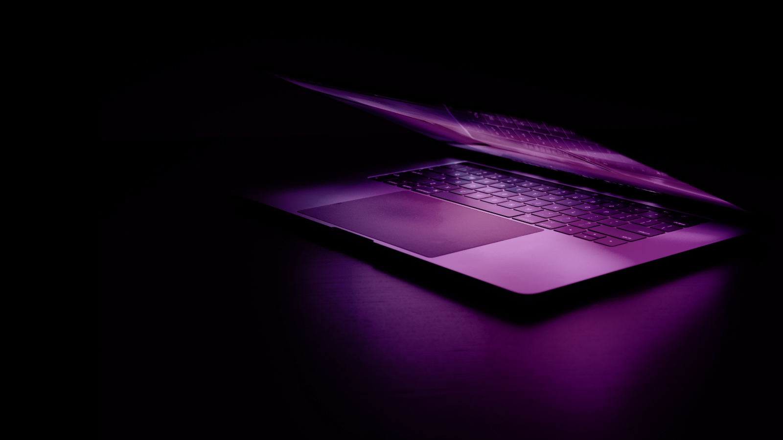 Un laptop viola brillantemente illuminato risplende nell'oscurità, mostrando la sua tonalità vibrante e il suo design elegante.